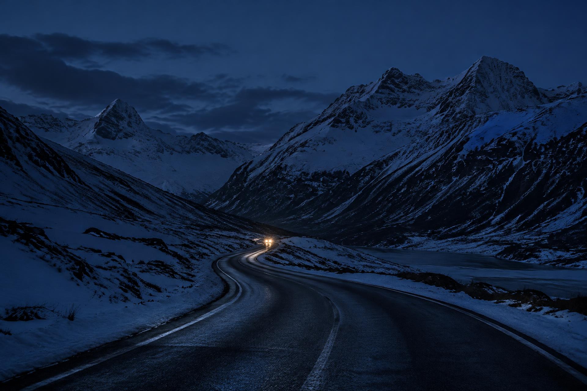 Route alpine enneigée de nuit, éclairée par des phares, entre sapins et sommets